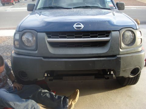 2004 Nissan Xterra - A mechanic works on the underside of a dark blue 2004 Nissan Xterra, captured from a front-facing perspective.