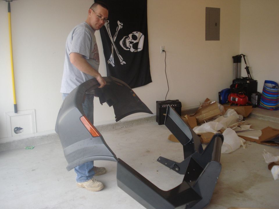 Gray car bumper with orange turn signal, held by a man in a garage