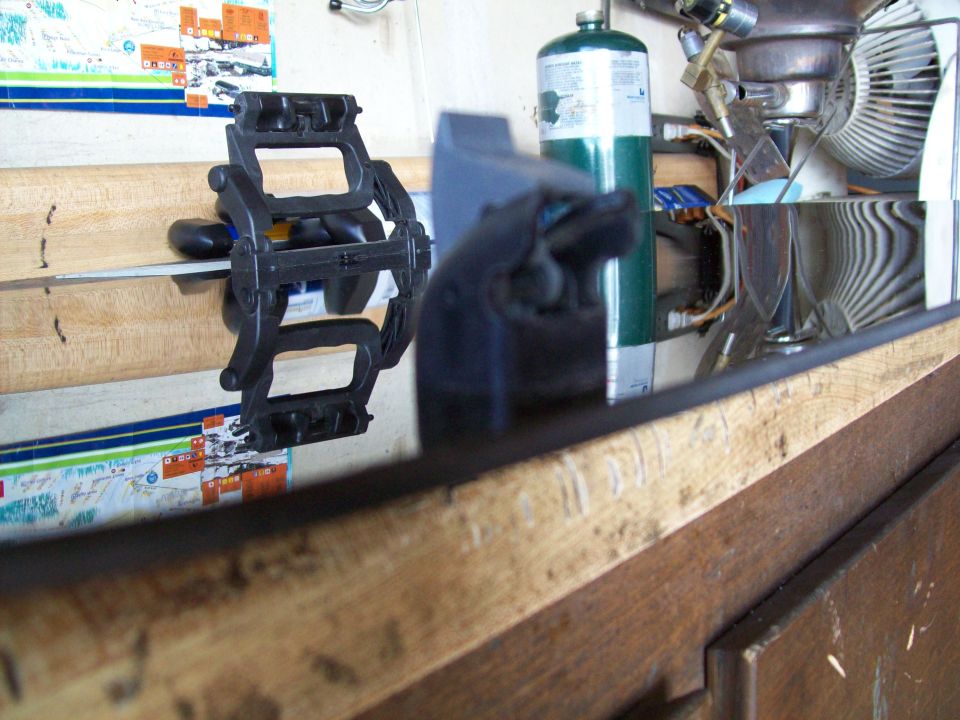 Black plastic clamp holding a metal rod on a wooden surface, with a propane tank and fan in the background