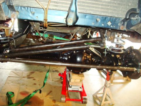 1995 Ford Bronco - Close-up view of the steering linkage and front axle assembly, supported by a hydraulic jack and jack stands.
