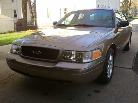 2007 Ford Crown Victoria - Tan 2007 Ford Crown Victoria parked in a driveway with a house and trees in the background.