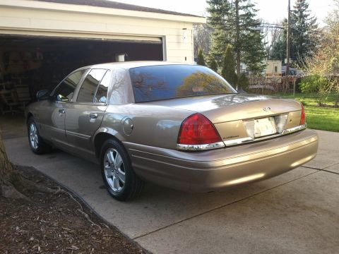 2007 Ford Crown Victoria - This tan sedan is parked in a driveway next to an open garage. The rear of the vehicle is visible.