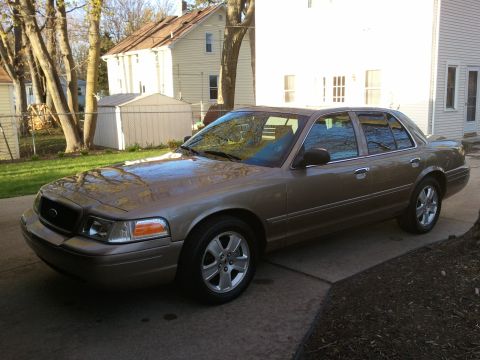 2007 Ford Crown Victoria - A tan 2007 Ford Crown Victoria sedan is parked on a concrete driveway in front of a residential house.