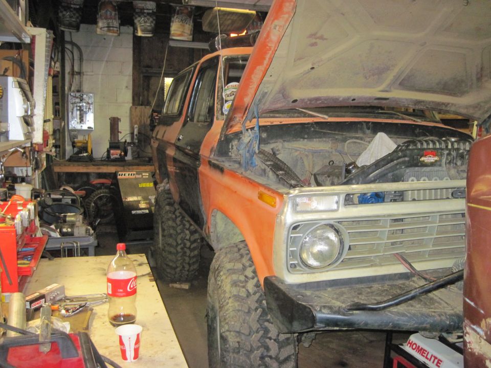 1978 Ford Bronco in garage, hood open, showing engine. Orange and black paint, lifted suspension