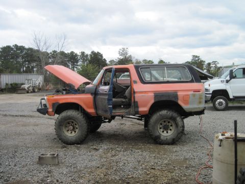 1978 Ford Bronco - Orange 1978 Ford Bronco undergoing work, with hood and door open. A white truck is parked nearby.