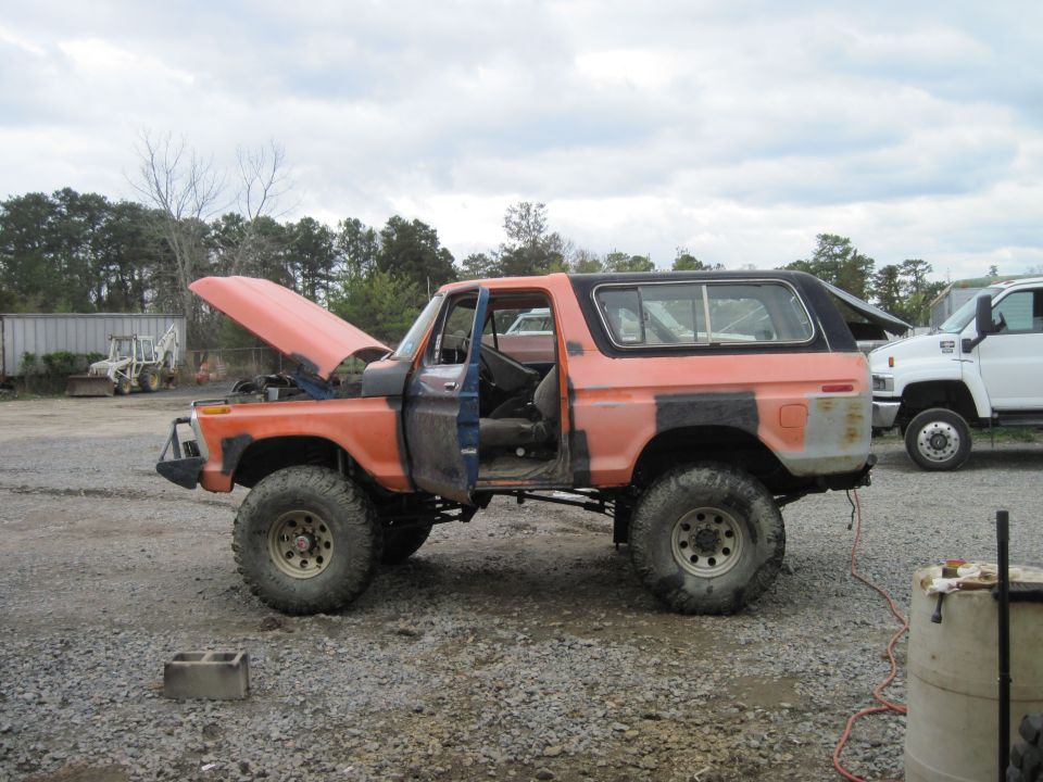1978 Ford Bronco with hood and driver door open, parked outdoors. Another white truck is visible in the background