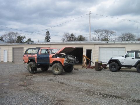 1978 Ford Bronco - A two-tone 1978 Ford Bronco sits outside a garage with its hood raised, while a white Jeep is parked nearby.