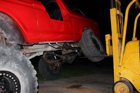 1978 Ford Bronco - A red 1978 Ford Bronco is being lifted by a yellow forklift, revealing its undercarriage and large tires.