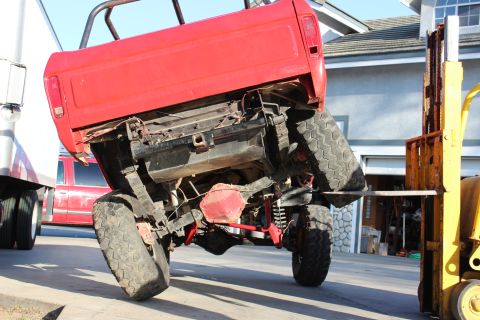 1978 Ford Bronco - A red pickup truck is being lifted by a yellow forklift, with another vehicle visible in the background.