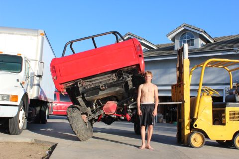1978 Ford Bronco - A person stands next to a red truck bed that is tilted upwards, with a white truck and a yellow forklift in the background.
