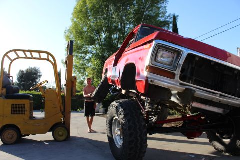 1978 Ford Bronco - A red 1978 Ford Bronco is being lifted by a forklift, revealing its modified suspension system.