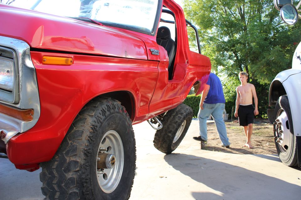 Red Ford Bronco with top and doors off on large off-road tires, low front angle