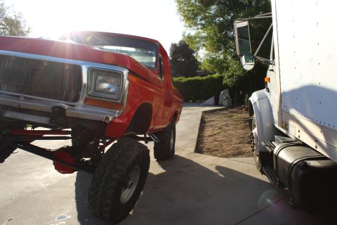 1978 Ford Bronco - A red pickup truck with significant lift and off-road tires is parked beside a white box truck.