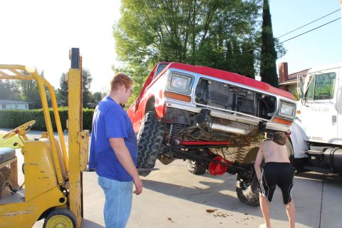 1978 Ford Bronco - Forklift lifting a red pickup truck. A white semi-truck is visible in the background.