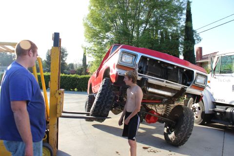 1978 Ford Bronco - A red pickup truck is being lifted by a forklift, with two people observing the process.