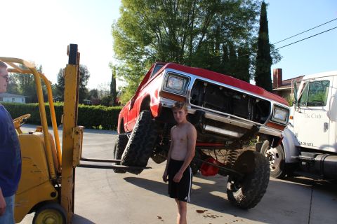 1978 Ford Bronco - A red lifted truck is being moved by a forklift, with a young man observing the operation.