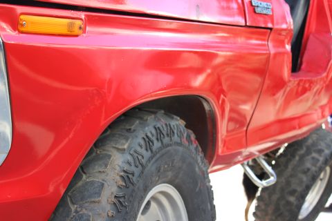 1978 Ford Bronco - Close-up side view of a red 1978 Ford Bronco, highlighting the fender, off-road tire, and the Bronco badging.