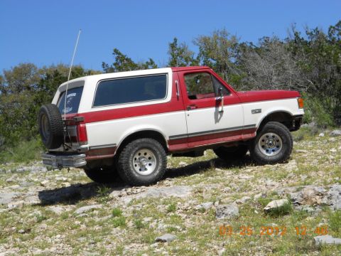 1989 Ford Bronco - Two-tone red and white 1989 Ford Bronco parked on a rocky hill under a clear blue sky.