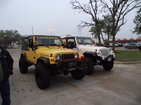 1989 Ford Bronco - Two modified Jeep Wranglers are parked in a lot under an overcast sky.