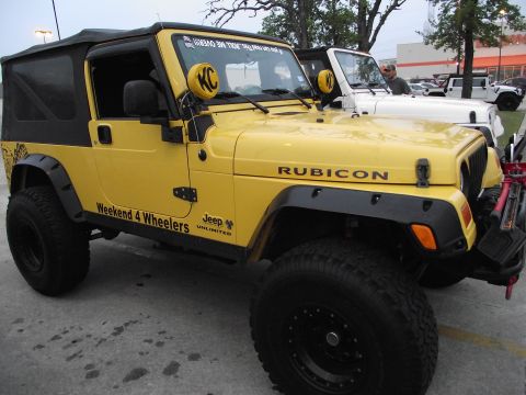 1989 Ford Bronco - A yellow Jeep Wrangler is parked next to a white Jeep Wrangler, with "RUBICON" visible on the hood.