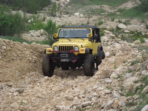 1989 Ford Bronco - Yellow Jeep Wrangler Rubicon navigates a rocky off-road trail.