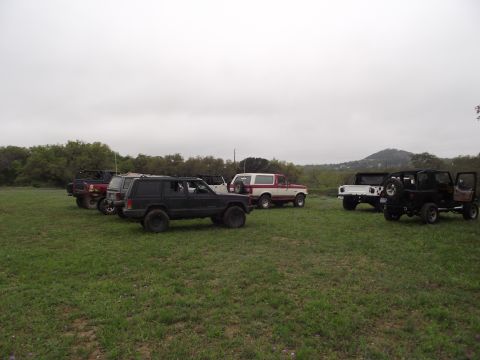 1989 Ford Bronco - A red and white 1989 Ford Bronco is parked in a grassy field alongside several other off-road vehicles.