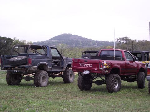 1989 Ford Bronco - Modified off-road vehicles, including a Toyota pickup and a dark SUV, are parked outdoors on a grassy area.