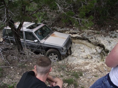 1989 Ford Bronco - A Jeep Cherokee XJ is stuck in a rocky ditch while onlookers observe the situation.