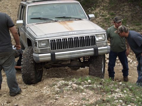 1989 Ford Bronco - Jeep Cherokee XJ on a dirt trail with two men observing the front of the vehicle.
