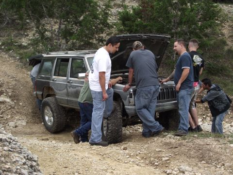 1989 Ford Bronco - A group of men are gathered around a lifted Jeep Cherokee XJ, appearing to work on it while off-roading.