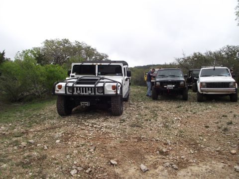 1989 Ford Bronco - A white Hummer H1 is parked in front of other off-road vehicles on a rocky terrain.