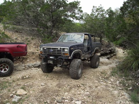 1989 Ford Bronco - Modified Ford Bronco on an off-road trail, with another truck nearby.