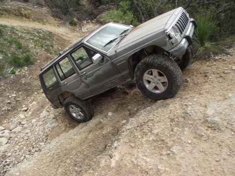1989 Ford Bronco - A gray Jeep Cherokee XJ navigates a steep, rocky trail, its off-road capabilities.