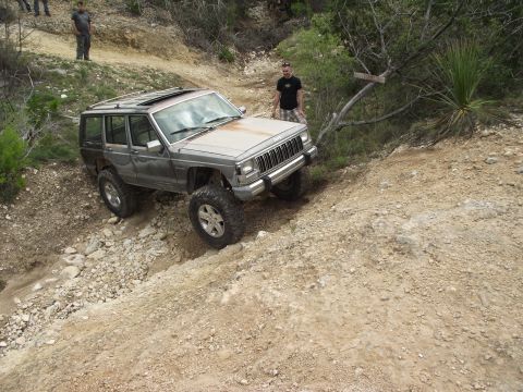 1989 Ford Bronco - A Jeep Cherokee XJ navigates a steep, rocky off-road trail with a person standing nearby.