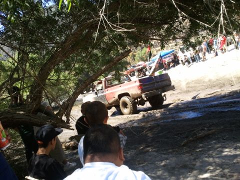 1978 Ford Bronco - Several off-road vehicles are gathered on a muddy slope, with one red and blue pickup truck prominently visible.
