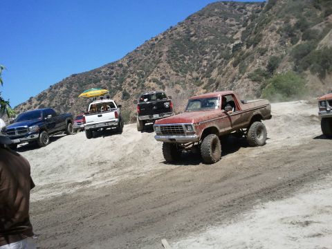 1978 Ford Bronco - A group of off-road trucks, including a lifted 1978 Ford Bronco, on a dusty trail.
