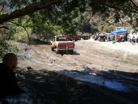 1978 Ford Bronco - A 1978 Ford Bronco navigates a muddy off-road course with other vehicles and spectators in the background.