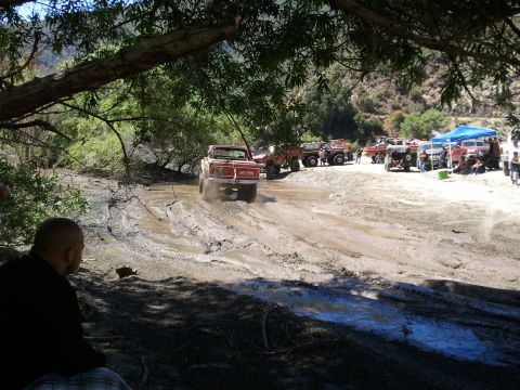1978 Ford Bronco - Off-road vehicles tackle a challenging muddy course with spectators watching.
