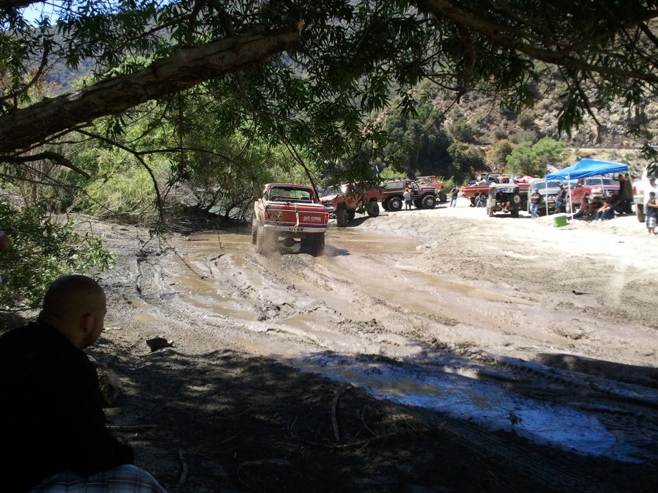 Several off-road trucks and ATVs navigating a muddy terrain under trees