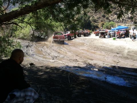 1978 Ford Bronco - A red 1978 Ford Bronco navigates a challenging muddy track with other vehicles and spectators present.