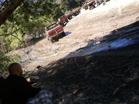 1978 Ford Bronco - Several off-road vehicles navigate a steep, muddy incline under a sunny sky.