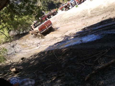 1978 Ford Bronco - Several trucks are seen struggling through a muddy terrain, with one vehicle in the foreground attempting to climb the climb.