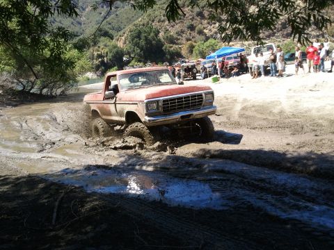1978 Ford Bronco - A red 1979 Ford F-150 pickup truck navigates a muddy off-road course with spectators in the background.
