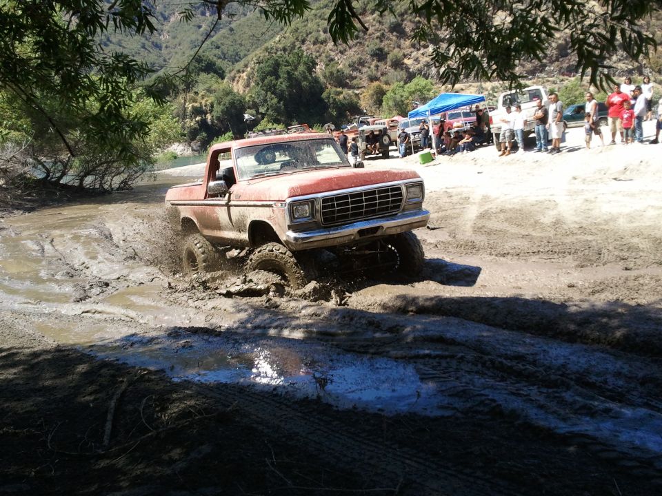 Red 1979 Ford F-150 pickup truck splashing through mud