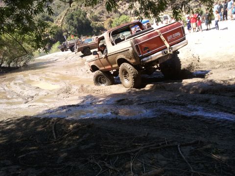 1978 Ford Bronco - Ford Bronco tackles a muddy trail with other vehicles following.