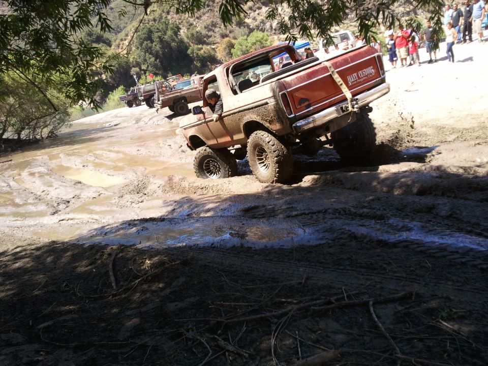 1978 Ford Bronco driving through mud with other trucks behind it