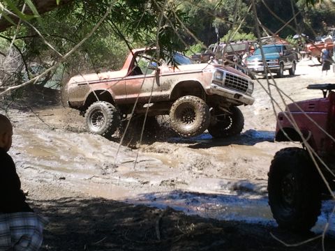 1978 Ford Bronco - This lifted truck navigates a challenging muddy terrain, with other off-road vehicles visible in the distance.