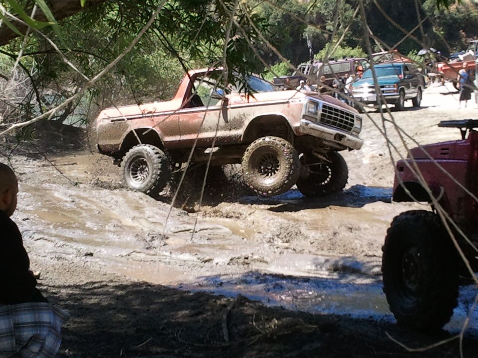 Muddy off-road truck climbing out of a ditch with other vehicles in the background