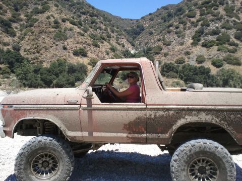 1978 Ford Bronco - A dirt-covered 1978 Ford Bronco drives through a rocky, mountainous terrain.