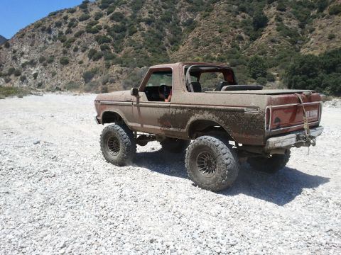 1978 Ford Bronco - A lifted 1978 Ford Bronco covered in mud navigates a rocky, off-road trail.